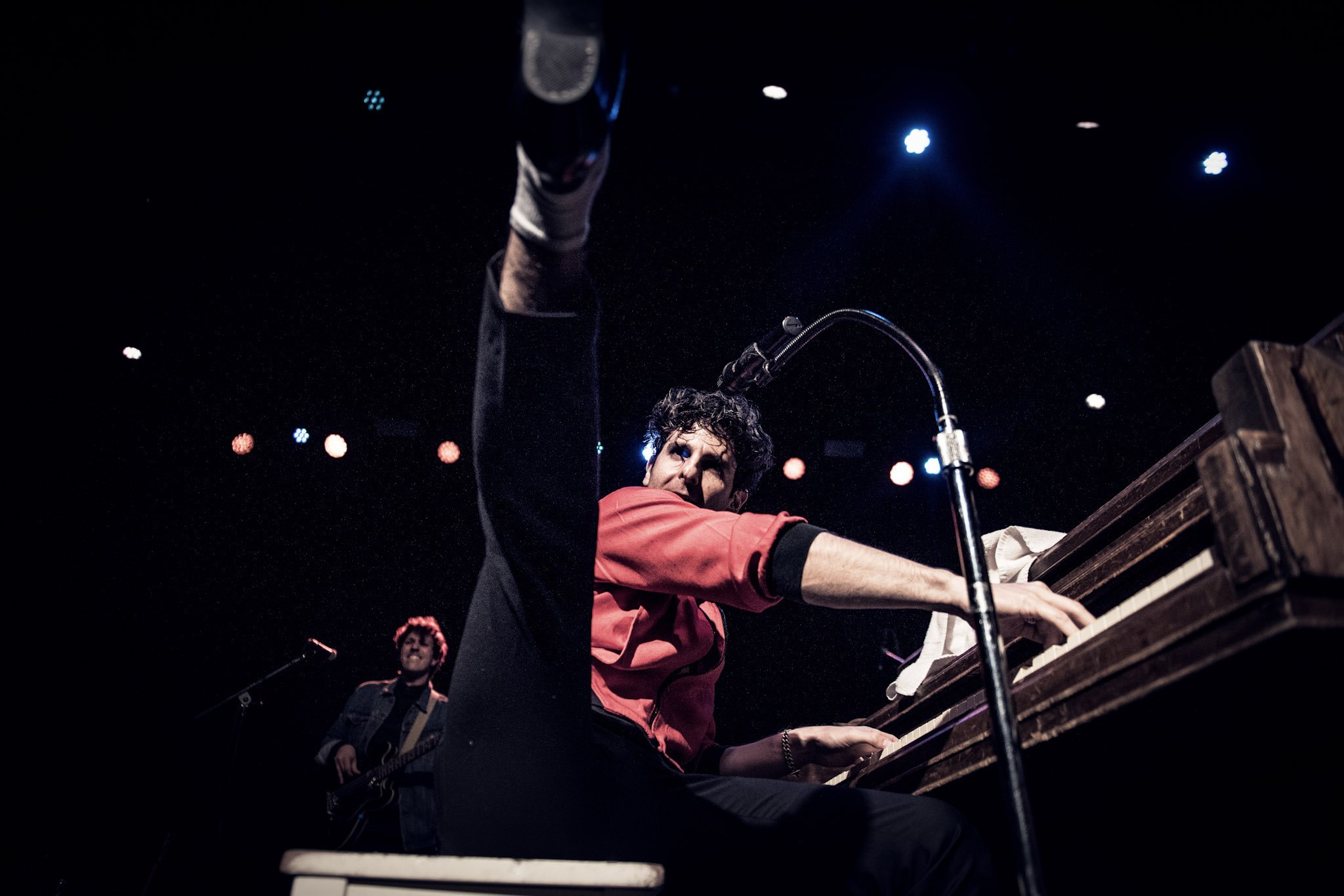 Adam Weiner kicking a leg over the piano, microphone arm curling overhead
